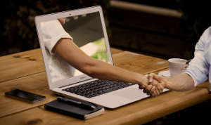 Arm reaching through a laptop to shake hands.